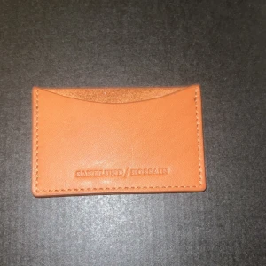 Korthållare sandlund/Hossain - Säljer ett stilrent orange kortfodral från Sandqvist. Perfekt för att hålla dina kort organiserade. Tillverkat i skinn med en enkel och elegant design. Passar perfekt i fickan eller väskan. Perfekt för vardagsbruk!
