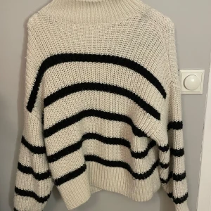 Randig stickad tröja från H&M - Säljer en supermysig stickad tröja från H&M i storlek M. Den är vit med svarta ränder och har en skön, oversized passform. Perfekt för höst och vinter! Tröjan har långa ärmar och en hög krage som håller dig varm. 🖤🤍