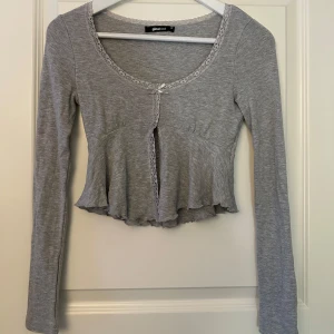 Grå långärmad topp från Gina Tricot - Säljer en superfin grå långärmad topp från Gina Tricot i storlek XS. Den har en söt volangdetalj och spetskant vid halsringningen. Perfekt för både vardag och fest! 💫