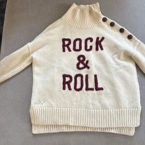 Vit stickad tröja från Zadig & Voltaire - Orginal pris 2000-3000 Säljer en supercool vit stickad tröja från Zadig & Voltaire med texten 'ROCK & ROLL' i mörkröd på framsidan. Tröjan har en hög krage och knappar längs axeln för en extra touch. Perfekt för höst och vinter, både mysig och stilren! 🖤