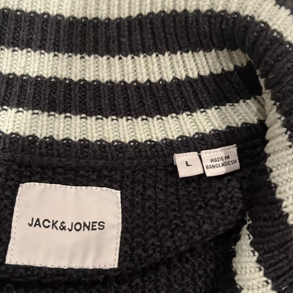 Säljer en snygg svart stickad tröja från Jack & Jones. Den har en dragkedja framtill och ett coolt märke på ärmen. Perfekt för höst och vinter med sin varma och bekväma design. Ribbad krage och muddar ger en extra touch. Passar både till vardags och lite finare tillfällen.. Tröjor & Koftor.