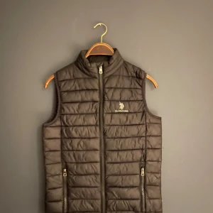 Svart dunväst från U.S. Polo Assn. - Säljer en svart dunväst från U.S. Polo Assn. i mycket bra skick. Västen har en dragkedja framtill och två praktiska fickor med dragkedjor. Perfekt för höst och vår när du vill hålla dig varm utan att bära en jacka. Stilren och enkel design som passar till det mesta.