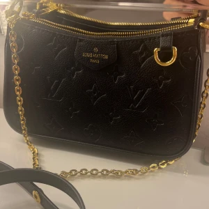 Svart axelväska från Louis Vuitton - Säljer en elegant svart axelväska från Louis Vuitton i skinn med det klassiska monogrammönstret. Väskan har en guldfärgad kedja och dragkedja, vilket ger en lyxig touch. Perfekt för både vardag och fest! LV Easy pouch on strap, både kedjan och långa bandet medföljer