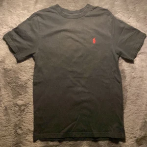 Svart t-shirt från Polo Ralph Lauren - Säljer en svart t-shirt från Ralph Lauren i storleken 10-12 som är runt 162 skulle jag säga! Den ganska använd men har inga fläckar vad jag har sett! Skriv för fler bilder eller frågor och funderingar!