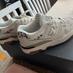 New Balance sneakers med leoparddetaljer - Säljer ett par snygga New Balance sneakers i vitt med coola leoparddetaljer. Skorna har en klassisk design med snörning och en bekväm sula. Perfekta för både vardag och festliga tillfällen! Inköpa på NK i somras💕