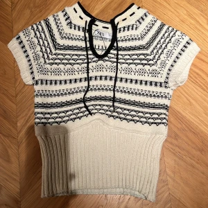 Mönstrad stickad topp från Zara - Säljer en superfin stickad topp från Zara i svart och beige. Den har ett snyggt mönster och korta ärmar. Perfekt för både vår och höst! Toppen har en ribbad nederdel och en knytning vid halsen för extra stilpoäng. Passar perfekt till jeans eller kjol. 🖤 Nyckick andvänd 1 gång, passar 11-14 åringar (själv på bilden är jag 13 år)