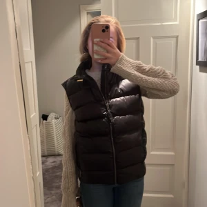 Svart dunväst från Parajumpers - Säljer en snygg svart dunväst från Parajumpers i mycket bra skick. Västen har en dragkedja framtill och är perfekt för höst och vinter. Den är vadderad och håller dig varm och stilren. Passar perfekt över en stickad tröja för en casual look.