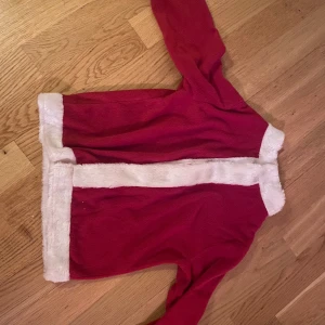 Röd juljacka med vit fuskpäls - Säljer en superfin röd jacka med vit fuskpälsdetalj, perfekt för julen! Den är i bra skick och har långa ärmar. Mysig och festlig för alla julfiranden. Passar perfekt för barn i storlek 110/120. 🎅🎄
