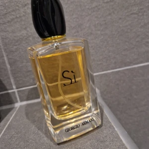 Parfym Si från Giorgio Armani - Säljer en elegant parfymflaska av märket Giorgio Armani, modell Si. Flaskan är genomskinlig med en svart kork och innehåller en gyllene doft. Perfekt för den som vill ha en lyxig och sofistikerad doftupplevelse. Flaskan rymmer 100 ml.