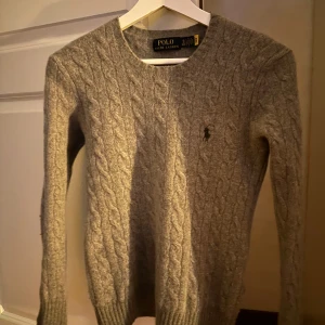 Grå stickad tröja från Polo Ralph Lauren - Säljer en snygg grå 100% kashmir tröja från Polo Ralph Lauren. Den har ett klassiskt flätmönster och är perfekt för kyliga dagar. Tröjan är i mycket bra skick och har långa ärmar. Passar perfekt för både höst och vinter. 🧶