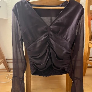 Lila långärmad topp med rynkdetaljer - Snygg lila topp med långa ärmar och rynkdetaljer framtill. Den har en v-ringad design och är tillverkad i ett lätt, transparent material. Använd fåtal gånger i storlek M.