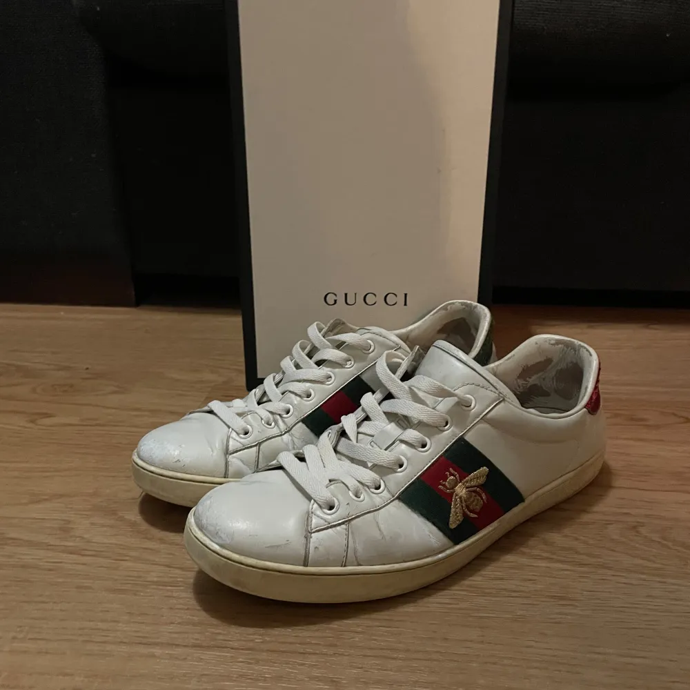 Säljer ett par stilrena vita sneakers från Gucci i bra skick. Skorna har den klassiska Gucci-randen i grönt och rött på sidan med en broderad insekt. Perfekta för både vardag och fest! Storlek 43. Används en del men fortfarnae mycket kvar att ge! Allt og medföljer!.. Skor.