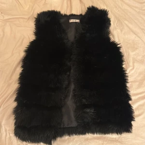 Svart pälsväst - Säljer en supermjuk och fluffig svart pälsväst. Perfekt för att hålla sig varm och stilren under kyliga dagar. Västen är i mycket bra skick och har en elegant design utan knappar eller dragkedja. Passar perfekt för både vardag och festliga tillfällen. Nypris 800kr och knappt använd 