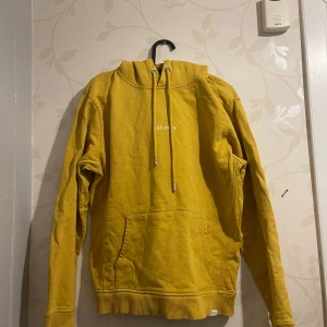 Gul hoodie från Les Deux - Säljer en snygg gul hoodie från Les Deux i bra skick. Den har en klassisk känguruficka och justerbar huva med snören. Perfekt för höst och vår när du vill vara både bekväm och stilren. Passar lika bra till skolan som till en chill dag hemma. Säljer pga fick den som en gåva men lite för stor för mig.