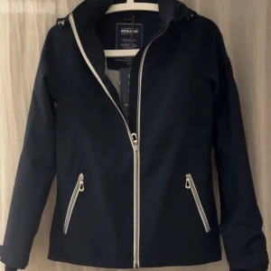 Marinblå jacka från Sebago - Säljer en marinblå Elena Performance Jacka från Sebago i storlek XS. Jackan har en snygg dragkedja och praktiska fickor med dragkedjor. Perfekt för höst och vår. Säljer pga att den var för liten och hann inte lämna tillbaka den. Jackan är bara testad och alla lappar är kvar. Hör av dig om du har någon fundering! 