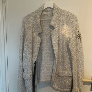 Kofta från Odd Molly - Säljer en snygg mönstrad kavaj i ljusgrått och vitt med ett coolt broderi på ärmen. Perfekt för höst och vår! Den har långa ärmar och en stilren design som passar både till vardags och fest. Kavajen är i bra skick och redo för en ny ägare. 🧥✨Storlek S/M. Odd mollys storlek 3