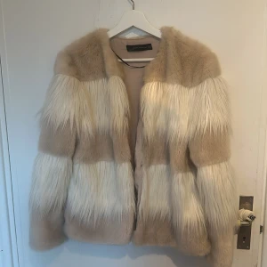 Beige och vit pälsjacka från Zara Woman - Säljer en superfin beige och vit pälsjacka från Zara Woman. Jackan har ett randigt mönster med långa ärmar och är perfekt för att hålla sig varm och stilren under kyliga dagar. Den är i mycket bra skick och passar perfekt för höst och vinter.