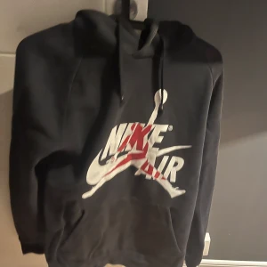 Svart Nike Air Jordan hoodie - Säljer en svart Nike Air Jordan hoodie med det ikoniska logotyptrycket på framsidan. Den har en stor luva och texten 'Air Jordan' längs ärmen. Den är i använt skick, är lite solblekt. Acceptabelt skick. 