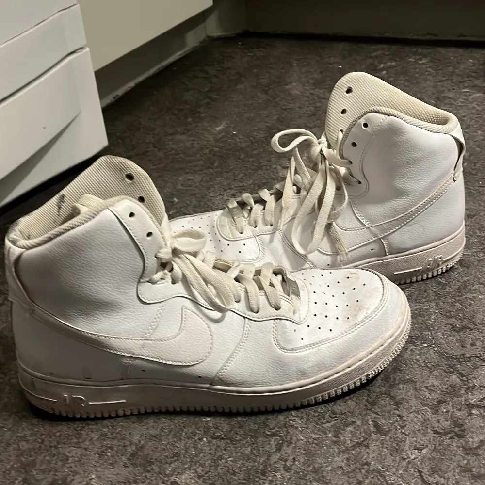 Säljer ett par vita Nike Air Force sneakers i helt okej skick. De har en klassisk hög modell med snörning och är perfekta för både vardag och fest. Skorna är bekväma och stilrena, men har lite smuts på sulan som lätt kan rengöras. Perfekta för dig som älskar streetwear!                          PRISET KAN DISKUTERAS!!🤍🩶🤍🩶. Skor.