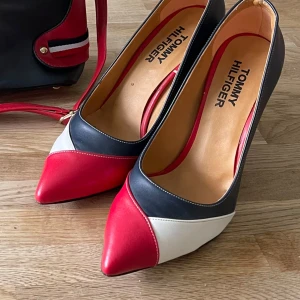 Färgglada pumps från Tommy Hilfiger - Snygga pumps köpt i Turkiet i somras i en vanlig butik så jag är osäkert på att de är original  Tommy Hilfiger. rött, blått och vitt. De har en spetsig tå och är perfekta för en festlig kväll. Skorna är helt nya aldrig använda.De har en elegant design som verkligen sticker ut.