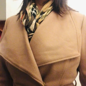 Beige kappa med bälte - Säljer en superfin beige kappa i ull med bälte i midjan. Den har en elegant krage och knäppning framtill. Perfekt för höst och vår, och ger en stilren look. Passar både till vardags och fest. 🧥✨