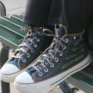 Blå sneakers med leopardmönstrade snören - Säljer ett par coola blå Converse sneakers i jeansmaterial med leopardmönstrade snören och nitar på baksidan! Perfekta för att ge din outfit en unik touch. 