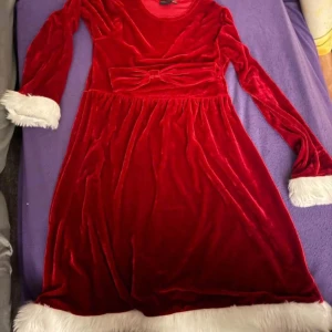 Röd jul klänning med hårband  - Säljer en superfin röd sammet klänning med vita fluffiga detaljer vid ärmslut och nederkant. Klänningen har långa ärmar och en söt rosett i midjan. Perfekt för jul och vintriga tillfällen! 🎅Medföljer ett rött hårband 