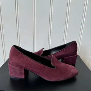 Vinröda mockaskor från Rizzo - Snygga vinröda mockaskor från Rizzo i storlek 36. De har en bekväm blockklack och en elegant design som passar perfekt för höst och vinter. Skorna är i mycket bra skick och har en stilren spetsig tå.