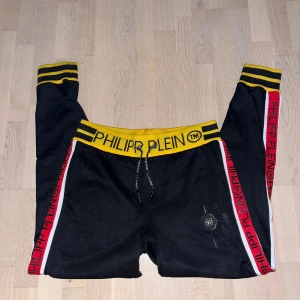 Svarta mjukisbyxor från Philipp Plein - Säljer ett par svarta mjukisbyxor från Philipp Plein i nyskick. De har en gul midja med logga och röda detaljer längs sidorna.  Kommer i originalförpackning, lappar och orderbekräftelse.🖤