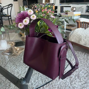 Vinröd handväska i skinn - Säljer en stilren vinröd handväska i skinn från ARKET. Väskan har en elegant design och en dragkedja inuti för säker förvaring. Köpt för 1990kr😊