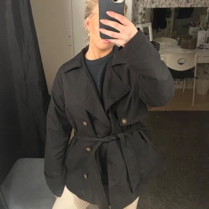 Svart kappa från Vero Moda - Säljer en snygg svart kappa från Vero Moda i storlek S. Den har ett bälte i midjan och knappar framtill för en stilren look. Perfekt för höst och vår, med långa ärmar och en klassisk design. Passar både till vardags och festliga tillfällen. 🖤