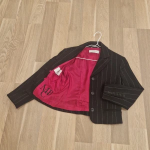 Svart randig kavaj och byxor från by Malene Birger - Snygg svart kavaj och byxor med vita ränder från by Malene Birger.Kavajen har en klassisk krage, tre knappar fram och en fin rosa insida. Byxorna är lite utsvängda och matchar perfekt med kavajen. Perfekt för en stilren look på kontoret eller en festlig tillställning. Ordinarie pris 5700:-