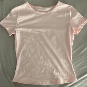 Ljusrosa t-shirt från Shein - Säljer en söt ljusrosa t-shirt från Shein. Den är i ett mjukt och stretchigt material, perfekt för vardagsbruk. T-shirten har en enkel design med korta ärmar och rund halsringning. Passar bra till både jeans och kjol!