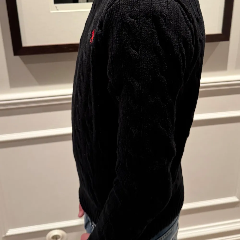 Säljer en snygg svart stickad tröja från Polo Ralph Lauren. Den har ett klassiskt flätmönster och en liten röd logga på bröstet. Den är i riktigt fint skick, modellen på bilden är 168cm och 52 kg. Tröjor & Koftor.