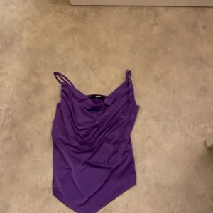Lila linnetopp från BikBok - Snygg lila linnetopp från BikBok i storlek S. Perfekt för sommardagar eller en utekväll. Toppen har smala axelband och en draperad design framtill som ger en stilren look. Materialet känns mjukt och bekvämt mot huden.