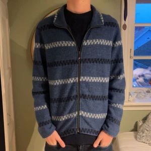 Blå randig kofta - Säljer en snygg och bekväm blå kofta med gråa ränder. Den har en praktisk dragkedja framtill och är perfekt för kyliga dagar. Koftan är i bra skick och passar både till vardags och lite finare tillfällen.