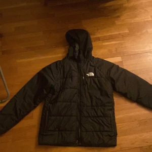 Svart pufferjacka från The North Face - Säljer en svart pufferjacka från The North Face i storlek XL barn. Jackan är perfekt för kalla dagar med sin quiltade design och huva. Den har en dragkedja framtill och är i mycket bra skick. Passar både höst och vinter. Perfekt för dig som vill hålla dig varm och stilren! 🖤