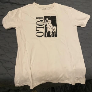 Vit t-shirt från Polo Ralph Lauren - Säljer en klassisk vit t-shirt från Polo Ralph Lauren i storlek xs. Den har ett coolt svart tryck med texten 'POLO' och en häst på framsidan. Perfekt för en avslappnad stil eller som basplagg i garderoben. T-shirten är i bra skick och gjord av mjuk bomull.