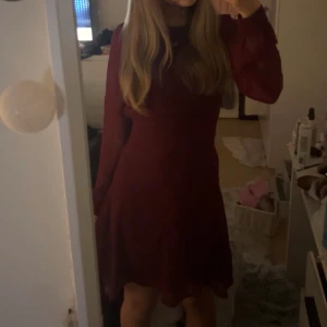 Vinröd klänning med öppen rygg - Säljer en elegant vinröd klänning i mycket bra skick. Den har långa ärmar och en snygg öppen rygg som ger en extra touch. Perfekt för höst och vinterfester. Klänningen har en normal passform och är superbekväm att bära. Rosetten går att knyta både i fram och bak beroende på vad man föredrar. 