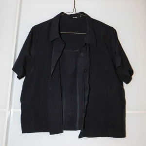 Svart kortärmad skjorta från Bik Bok - Säljer en stilren svart kortärmad skjorta från Bik Bok i storlek M. Skjortan har en klassisk krage och knappar framtill. Perfekt för både vardag och festliga tillfällen. Passar bra till jeans eller kjol för en avslappnad look.