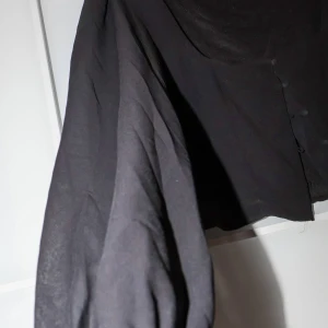 Svart blus från Gina Tricot - Säljer en elegant svart blus från Gina Tricot. Den har långa ärmar och knappar framtill som ger en stilren look. Perfekt för både vardag och fest. Passar bra till jeans eller kjol för en chic outfit!