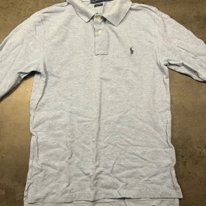 Ljusblå pikétröja från Ralph Lauren - Säljer en stilren ljusblå pikétröja från Ralph Lauren. Tröjan har långa ärmar och klassisk krage med knappar. Perfekt för både vardag och lite finare tillfällen. Den är i bra skick och redo för en ny ägare! Nypris överallt är 1500:-