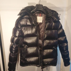 Svart Moncler Maya - Säljer en snygg svart pufferjacka från Moncler Maya i mycket bra skick. Det är storlek 1 men passar storlek M. Perfekt för att hålla sig varm och stilren i kylan! NFC scan funkar