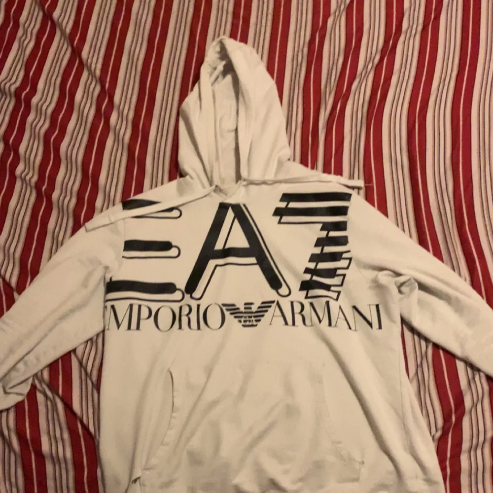 Säljer en snygg vit hoodie från Emporio Armani med stor logga på framsidan. Den är i bra skick och perfekt för både vardag och chill. Hoodien har en klassisk passform med långa ärmar och en skön huva. Perfekt för höst och vår! Den är också skön för Vintern nu när det börjar bli kallt. Den finns 2 små hål på båda sidorna av fickan men lite tråd går det o fixa. Den är storlek Medium/Large. Jag köpte den för cirka 2500 men pris går och diskuteras också.. Hoodies.