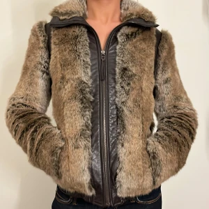Brun pälsjacka med dragkedja - Säljer en supermysig brun pälsjacka med dragkedja. Jackan har en snygg kombination av äkta päls och skinn, vilket ger den en unik look. Perfekt för kyliga höst- och vinterdagar. Den har långa ärmar och en normal passform. Perfekt för att hålla sig varm och stilren!