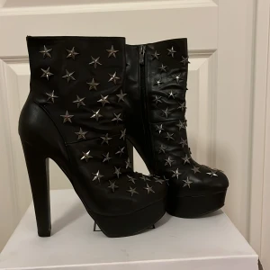 Svarta boots med stjärndetaljer från NLY - Snygga svarta boots i skinn från NLY med coola stjärndetaljer i silver. De har en hög klack och dragkedja på sidan för enkel på- och avtagning. Perfekta för en utekväll eller fest! Skorna är i mycket bra skick och redo att rocka din outfit ⚡️🪩