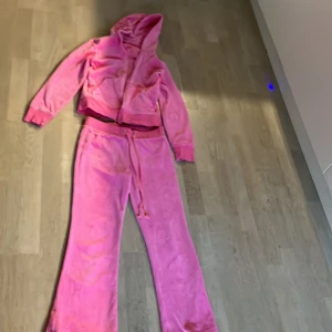 Rosa mjukisbyxor med matchande hoodie - Säljer ett set med rosa mjukisbyxor och en matchande hoodie. Byxorna har en loose passform med fickor bak och snörning i midjan. Hoodien har dragkedja och en mysig huva. Perfekt för chill dagar hemma eller en avslappnad stil ute. Materialet är mjukt och bekvämt. Går att göra längre då jag har sytt upp dom och då passar den någon som är runt 155cm