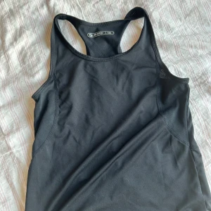 Svart träningslinne från SOC - Säljer ett svart träningslinne från SOC i mycket bra skick. Perfekt för träning med sin bekväma passform och ärmlösa design. Materialet är lätt och andas bra, vilket gör det idealiskt för intensiva pass. Passar både inomhus och utomhusaktiviteter.