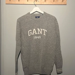 Grå stickad GANT tröja, 100% lammull - Säljer en stilren grå ull tröja från GANT i storlek S. (100% lammull) Den har ett klassiskt tryck med 'GANT 1949' på bröstet. Tröjan är i mycket bra skick och perfekt för både höst och vinter. Den är långärmad och gjord i ett mycket mjukt material som håller dig varm. Perfekt att ha till vardags men även till finare tillfällen. Öppen för byten. Pris kan diskuteras vid snabb affär.