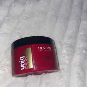 Bild på en röd burk från Revlon Professional, Uniq One All In One Hair Mask. Burken har ett svart lock och innehåller 300 ml produkt. Perfekt för att vårda och återfukta håret.